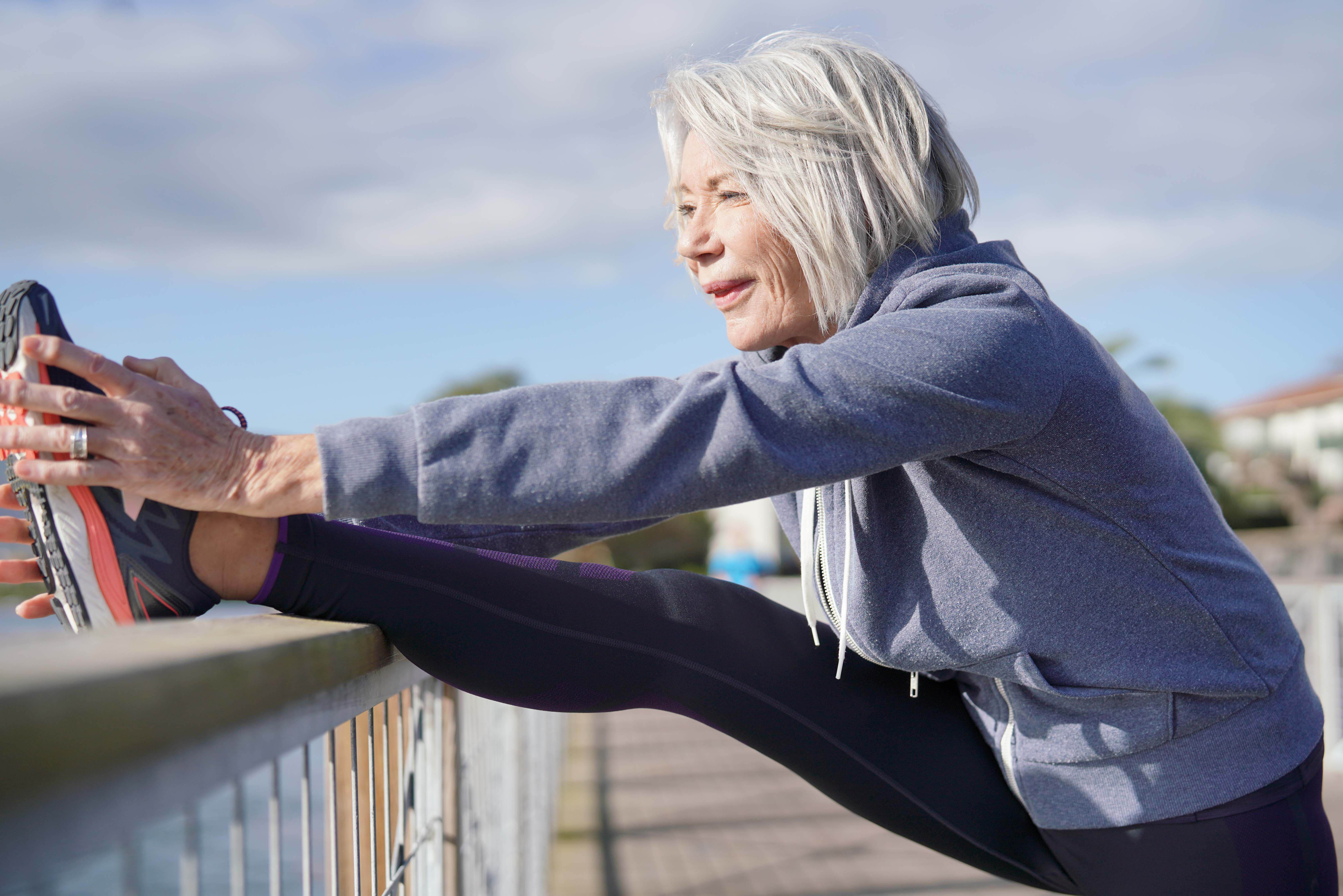 Older woman stretching her leg on a railing near the water